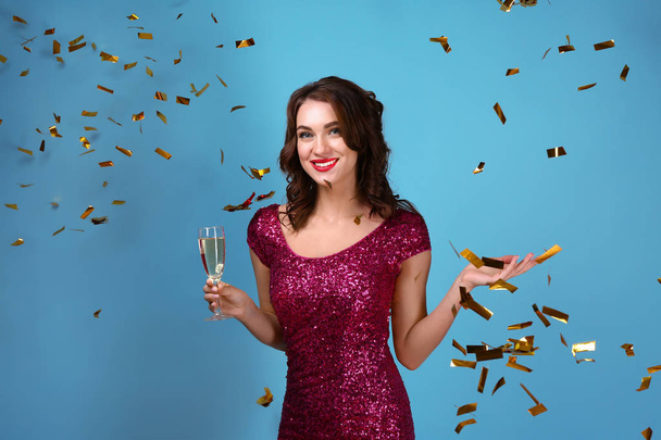 Beautiful young woman with glass of champagne and falling confetti on color background - Фото, зображення