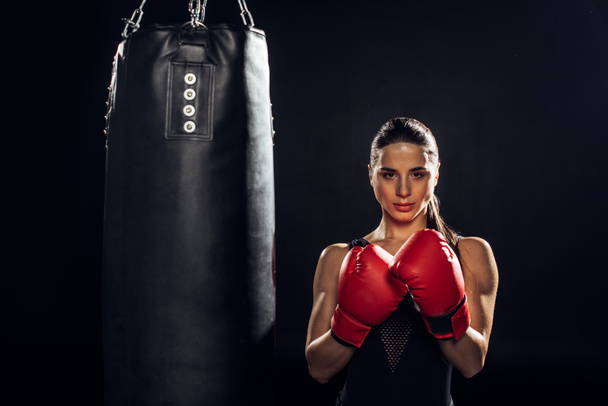 Vue de face du boxeur en gants de boxe rouges debout près d'un sac de boxe sur fond noir
 - Photo, image