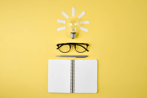 Financial planning table top with pen, notepad, eyeglasses and light bulb on yellow background. Concept brainstorming and new idea - Valokuva, kuva