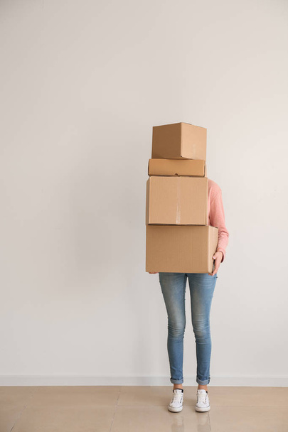 Vrouw met bewegende dozen in de buurt van lichte muur in de kamer - Foto, afbeelding
