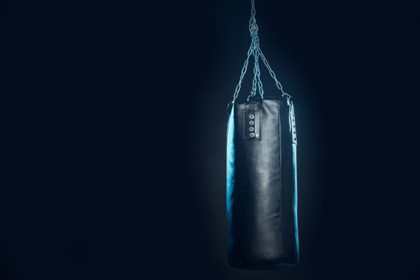 Leather punching bag hanging on steel chains on black - Zdjęcie, obraz