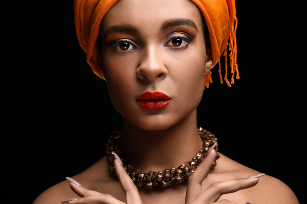 Portrait of beautiful African-American woman with head scarf on dark background - Photo, Image