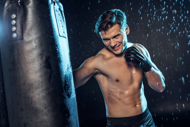 Boxeador de entrenamiento con saco de boxeo bajo gotas de agua en negro
 - Foto, imagen