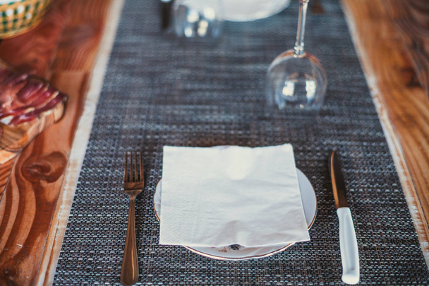 heller Holztisch: weiße Teller, rustikales dunkles Tischtuch mit Salami, Käse, Wein und Schinken. Ansicht von oben. - Foto, Bild