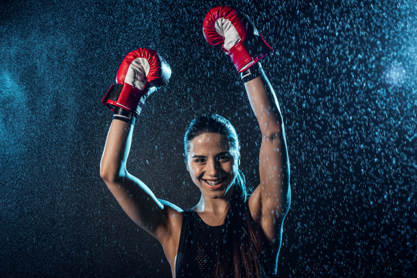 Smiling boxer in red boxing gloves showing yes gesture under water drops on black - Photo, Image