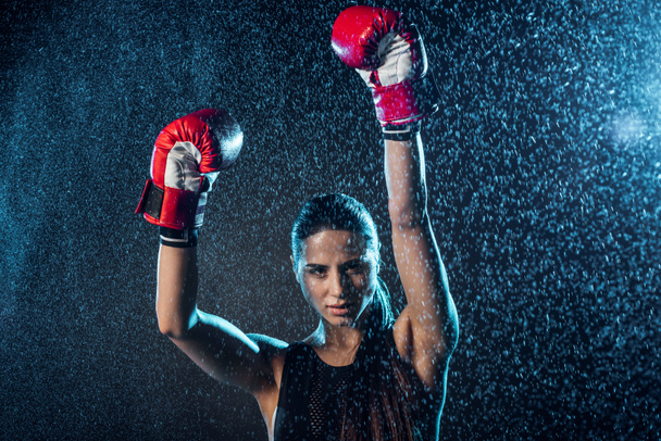 Boxer in red boxing gloves showing yes gesture under water drops on black - Foto, immagini