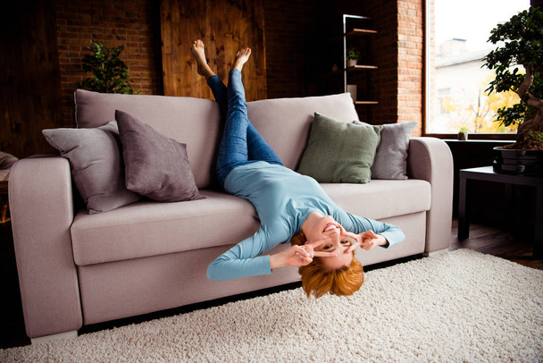 Full length body size photo beautiful she her lady hands arms legs raised upside down show v-sign eyes best day wear blue casual pullover jeans denim sit comfy couch divan house living room indoors - Foto, Imagem