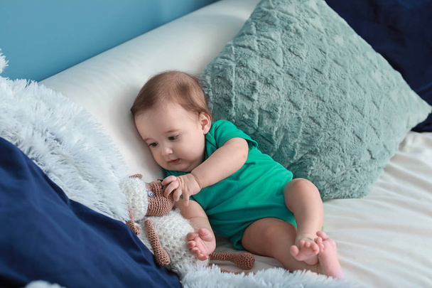 Adorable bebé con juguete sentado en un sofá suave en casa
 - Foto, Imagen