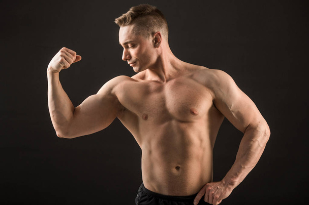 handsome muscular man on black background showing biceps - Фото, зображення