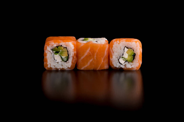 Japanese traditional food - sushi with avocado, rice, cottage cheese, salmon and green onion on the black background - Photo, image