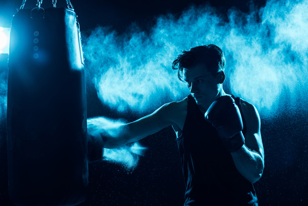Boxer concentré dans l'entraînement des gants de boxe avec sac de boxe dans l'obscurité
 - Photo, image