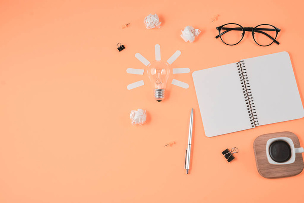 Flat lay financial planning brainstorming messy table top image with blank clip board, office supplies, pen, notepad, eyeglasses, cup of coffee, light bulb on orange background. - Foto, imagen