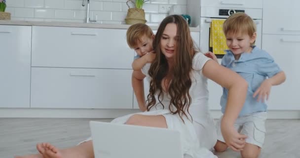 現代の技術。モダンなアパートメントの愛するママとリビング ルームの床の上に座って 2 人の小さい息子は、ノート パソコンの画面を見てください。お母さんと子供たちがラップトップでプレーします。. - 映像、動画