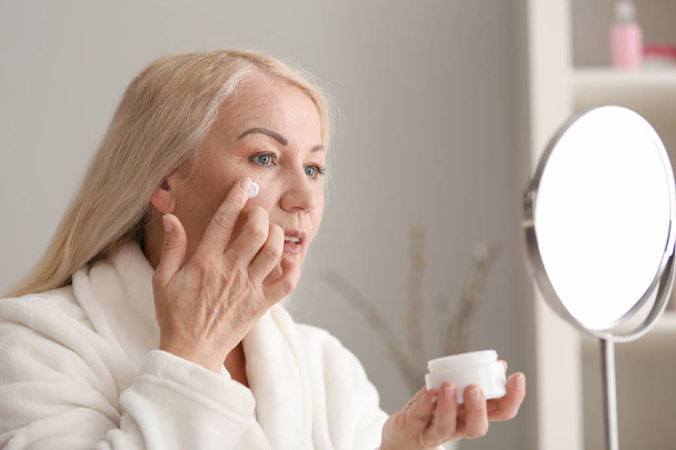 Mature woman applying facial cream at home - Photo, Image