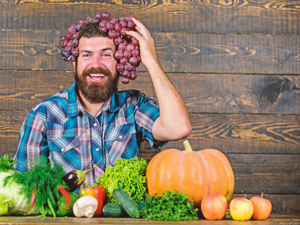 Grapes from own garden. Farming concept. Farmer proud of grapes harvest. Man hold grapes wooden background. Farmer bearded guy with homegrown harvest grapes put on head. Fresh organic harvest - Zdjęcie, obraz