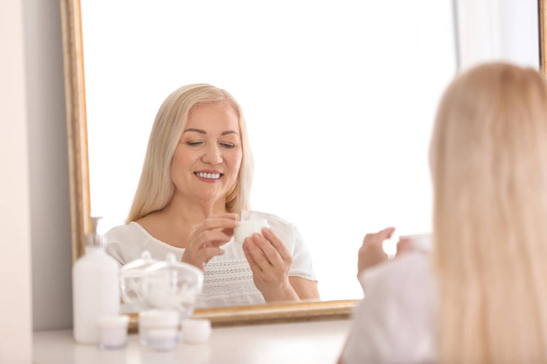 Mujer madura aplicando crema facial en casa
 - Foto, imagen