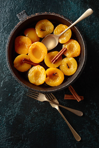 Peach dessert with cinnamon and cloves on a dark background. - Photo, Image