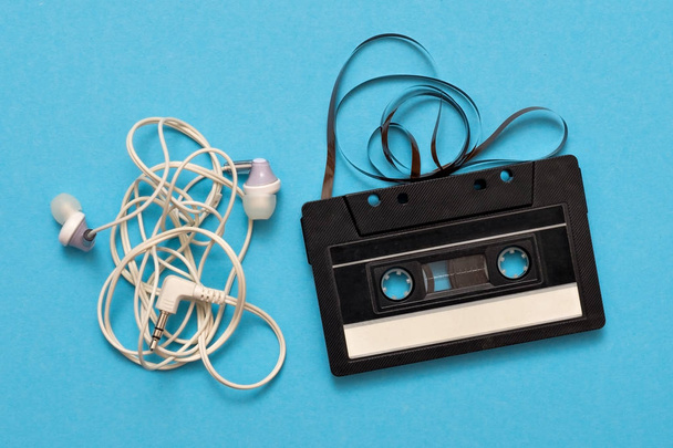 tangled earphones and retro music cassette isolated on blue background. - Photo, Image