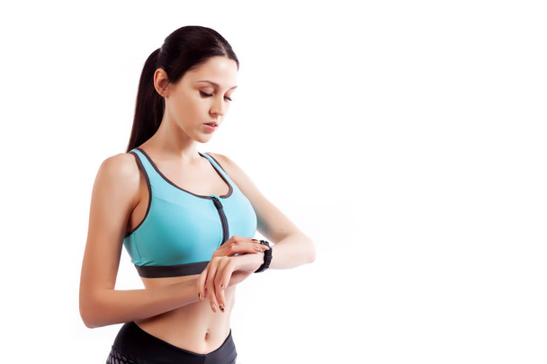 Nádherné fitness žena looing na hodinky na bílém pozadí izolované ve studiu. Fit girl aktivní život - Fotografie, Obrázek