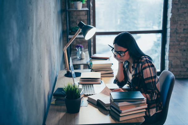 Profile side view of nice attractive smart clever intelligent brunette lady in checked shirt researching marketing materials pile stack at industrial loft style interior work place station - Foto, Imagen
