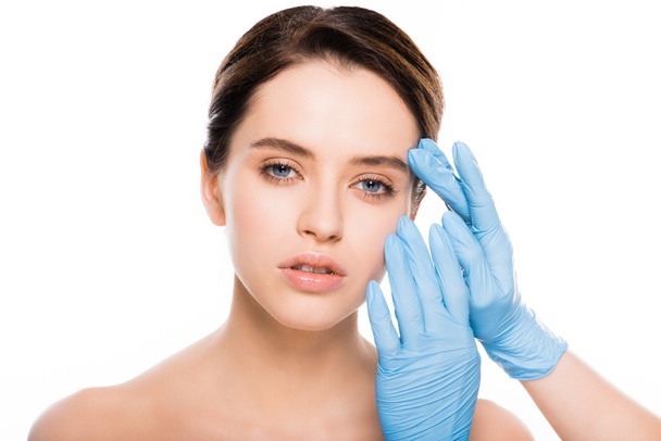 обрезанный вид пластического хирурга в латексных перчатках трогательное лицо брюнетки женщина изолированы на белом
 - Фото, изображение