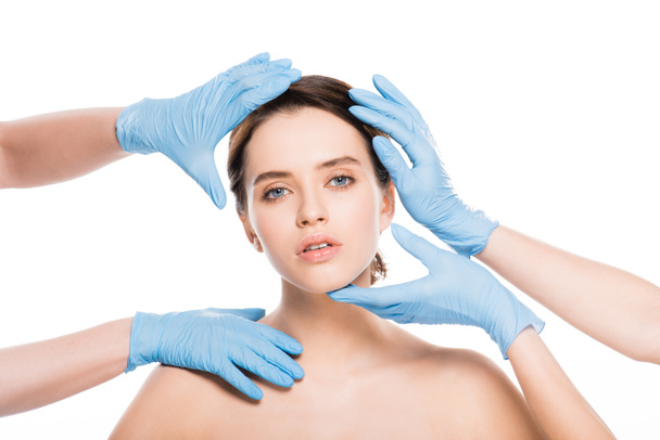 abgeschnittene Ansicht von plastischen Chirurgen in blauen Latex-Handschuhen berühren Gesicht von nackten Mädchen isoliert auf weiß - Foto, Bild