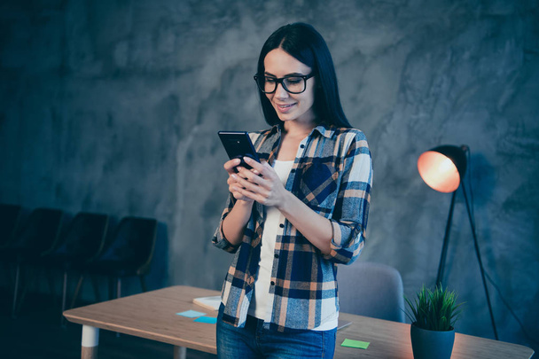 Portrait of her she nice-looking cute lovely attractive charming sweet cheerful cheery brunette lady wearing checked shirt reading sms at industrial loft style interior work place station - Foto, imagen
