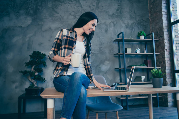 Low below angle view of nice cute lovely attractive charming sweet cheerful brunette lady wearing checked shirt free time browsing at industrial loft style interior work place station - Foto, Bild