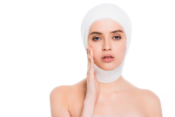 naked girl with bandaged head touching face after plastic surgery isolated on white  - 写真・画像