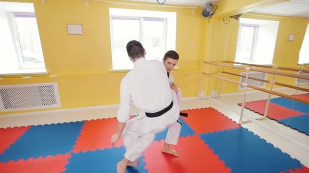Martial arts. Two athletic men training their aikido skills in the studio. Protecting from a leg hit and throwing the opponent on the floor - Footage, Video