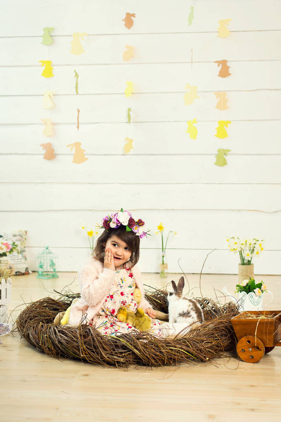 A happy little girl in a dress with flowers on her head is sitti - Φωτογραφία, εικόνα