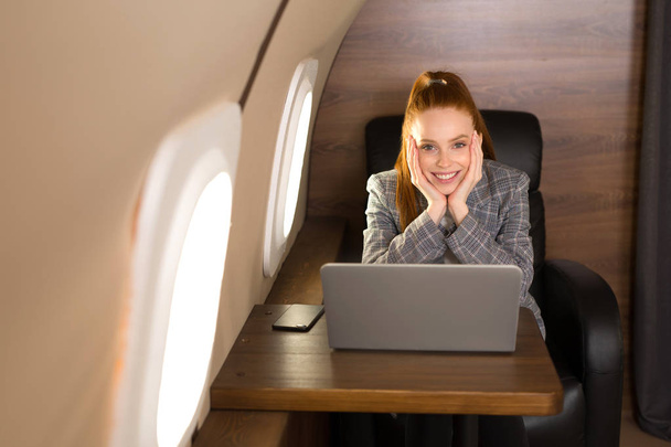  beautiful young girl with red hair is flying in a business class plane with a laptop - Foto, imagen