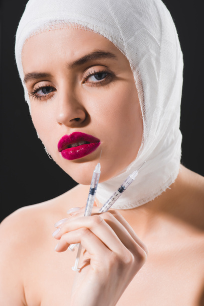 attractive young woman with bandaged head holding syringes isolated on grey  - Foto, imagen