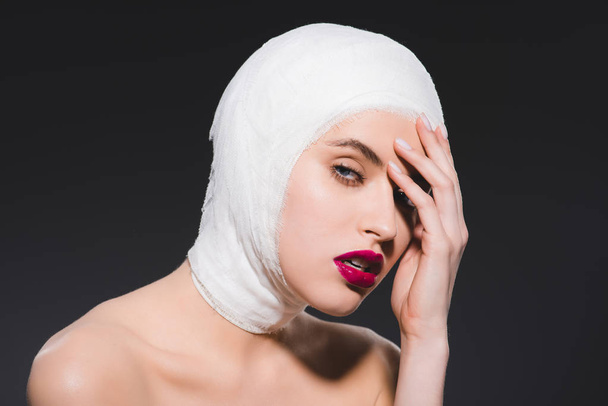 junge Frau mit purpurroten Lippen und bandagiertem Kopf isoliert auf grau  - Foto, Bild