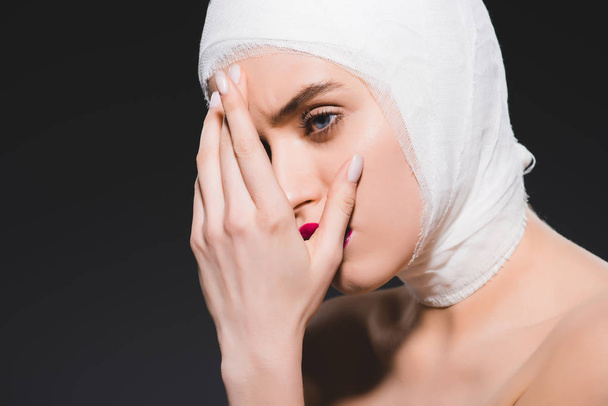 Młoda kobieta z bandażach głowy pokrycie twarzy izolowane na szarym  - Zdjęcie, obraz