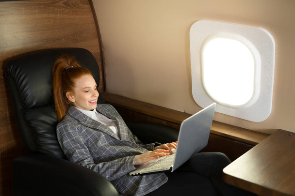 beautiful young girl with red hair is flying in a business class plane with a laptop - Foto, immagini