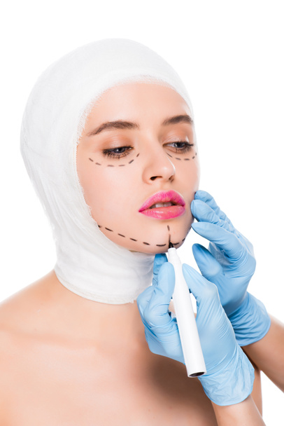 cropped view of plastic surgeon in latex gloves holding marker pen near woman with marks on face isolated on white  - Photo, Image
