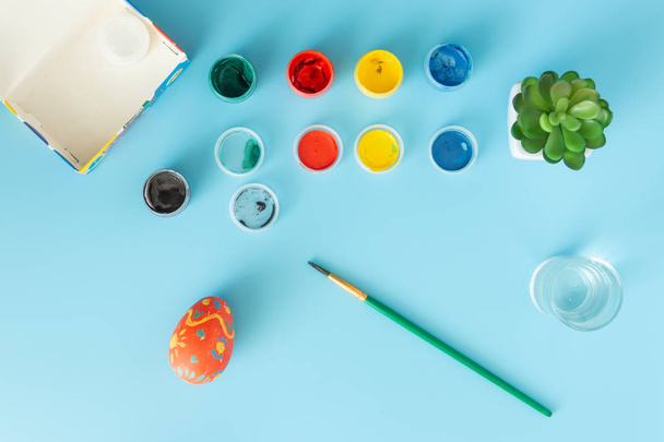 Příprava na velikonoční vícebarevné barvy a ručně vyrobené barevné vajíčko vedle kartáčku na modrý bacground velikonoční koncept - Fotografie, Obrázek