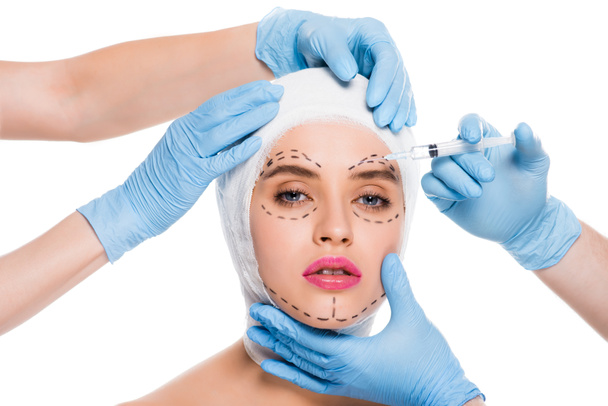 cropped view of plastic surgeons in blue latex gloves with syringe near face of woman with marks isolated on white  - Fotó, kép