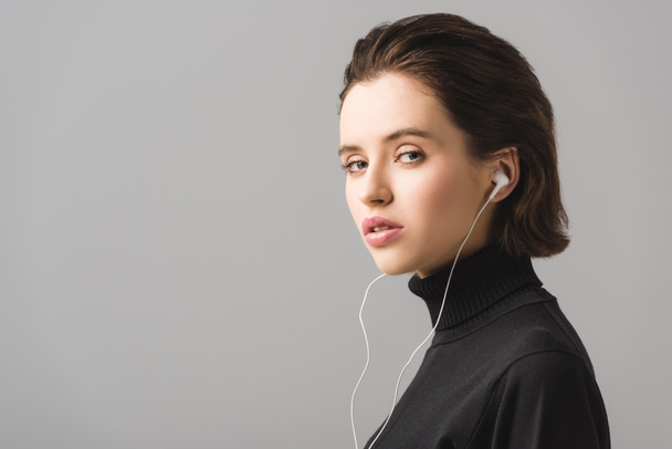 young woman in black jumper listening music in earphones isolated on grey  - Fotó, kép