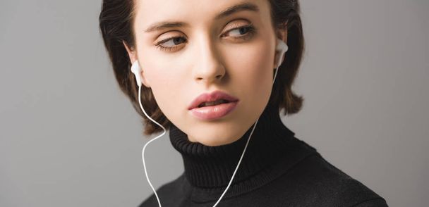 panoramic shot of woman in black jumper listening music in earphones isolated on grey  - Foto, Imagem