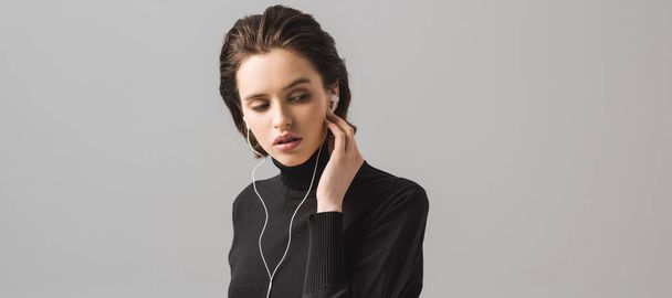 panoramic shot of girl in black jumper listening music in earphones isolated on grey  - Fotografie, Obrázek