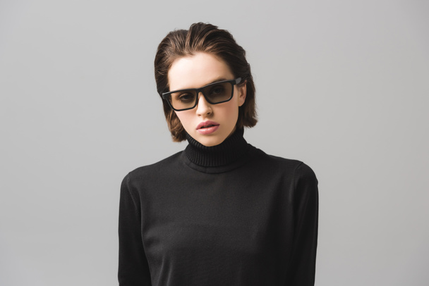 aantrekkelijke jonge vrouw in zwarte trui en zonnebrillen geïsoleerd op grijs  - Foto, afbeelding