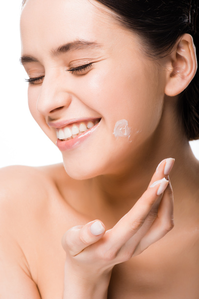 fröhliche nackte junge Frau, die kosmetische Creme isoliert auf Weiß aufträgt  - Foto, Bild
