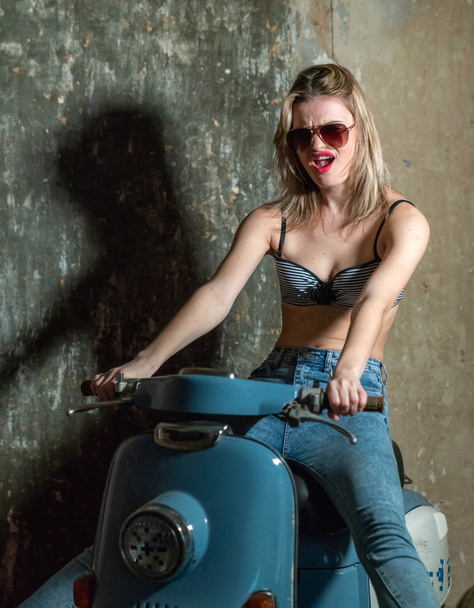 Beautiful young girl in a bodice and jeans in on a scooter - Фото, зображення
