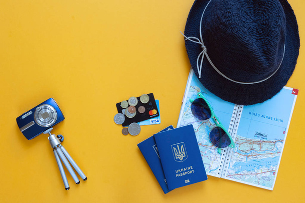 黄色の背景に旅行するもの: 青いパスポート、地図、お金、クレジットカード、帽子、サングラス、フォトカメラと三脚、上からの眺め、水平フレーム - 写真・画像