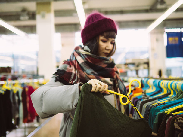 Mujer joven está navegando por un carril de ropa en la tienda del centro comercial
 - Foto, Imagen