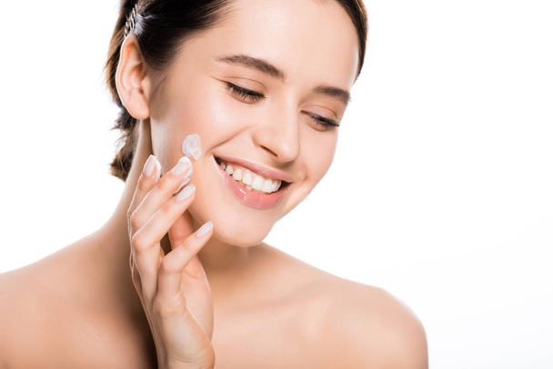 happy naked brunette woman applying face cream isolated on white  - Fotó, kép