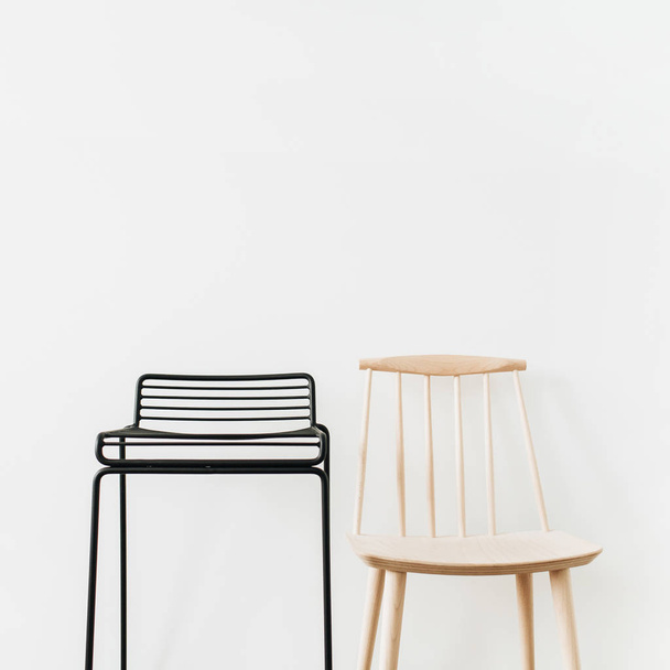 Black metal stool, wooden chair at white wall. Modern minimal Scandinavian furniture design concept. - Фото, изображение
