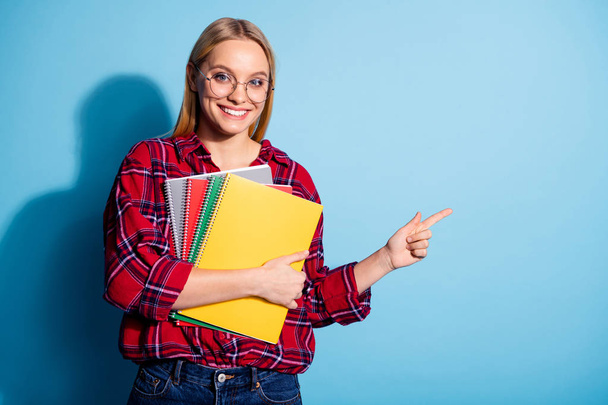 Portrait of her she nice charming cute attractive cheerful teen girl wearing checked shirt holding in hands copy-book pointing aside ad isolated over teal turquoise bright vivid shine background - 写真・画像